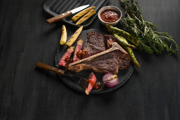 Cooking steak porterhouse with vegetables on a plate and pan grill. Black table background. Copy text area for menu design. 