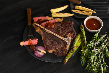 Porterhouse with vegetables on a plate and pan grill. Black table background with brown textile. Copy text area for menu design. Horizontal top view, flat, overhead.
