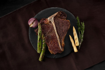 Grilled beef steak sliced lying on a plate and pan grill. Black table background with brown textile. Copy text area for menu design. Horizontal top view, flat, overhead.
