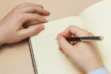 Close up of casual man writing on paper notebook or old diary
