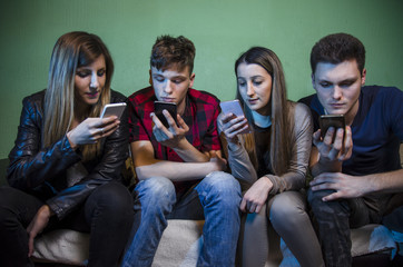 Group of teenagers and young adults staring at smartphones and not communicating with each other, anti social concept. Selective focus on girl on the right 