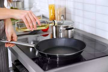 Closeup of woman pouring oil on frying pan