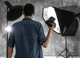 Young male photographer in studio with professional lighting equipment
