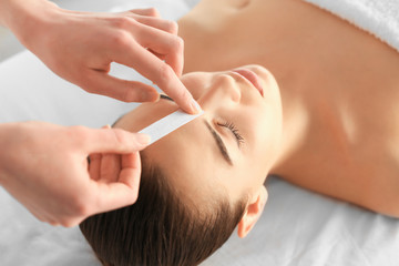 Obraz na płótnie Canvas Beautician waxing young woman's eyebrows in spa center