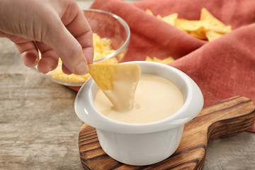 Female hand dipping nacho in bowl with beer cheese dip, closeup