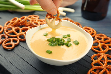 Female hand dipping pretzel in bowl with beer cheese dip, closeup