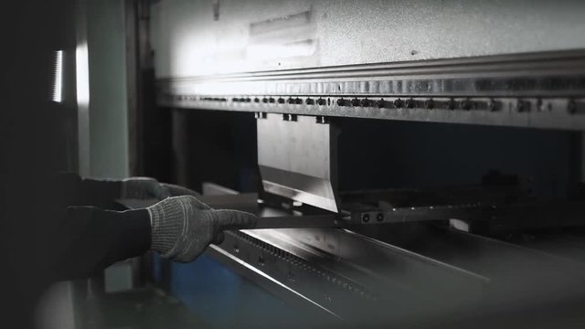 Worker bends a metal plate on the industrial machine for furniture line