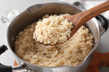 Spoon with prepared brown rice over saucepan