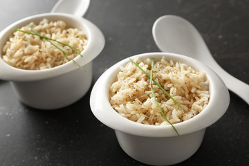 Two bowls with brown rice on gray table background
