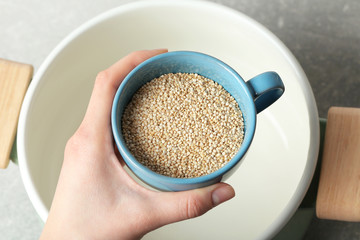 Female hand holding cup with quinoa seeds over saucepan