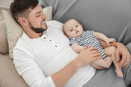Father lying with cute baby daughter on sofa at home