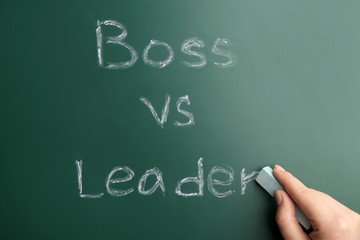 Female hand with chalk and words BOSS VS LEADER on chalkboard