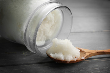 Spoon with fresh coconut oil taken from glass jar on wooden background