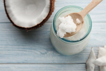 Spoon with fresh coconut oil taken from glass jar on light wooden background