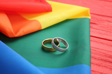 Two wedding rings and rainbow gay flag on wooden background