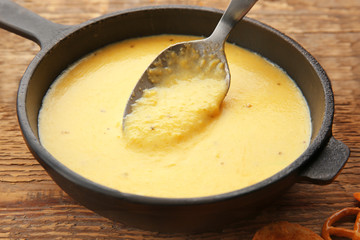Frying pan of creamy cheese with spoon on wooden background