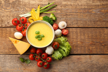 Appetizing composition of creamy cheese in bowl and fresh vegetables on wooden background