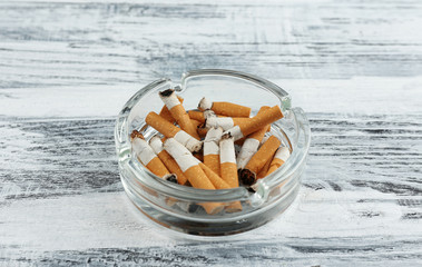 Glass ashtray with cigarette butts on wooden background