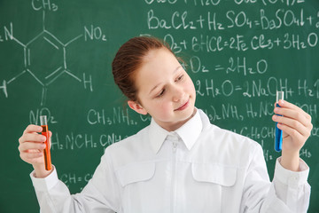 Beautiful school girl holding tubes on chalkboard background in chemistry class