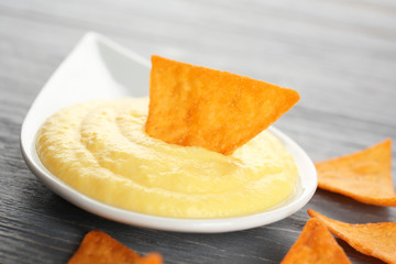 Dipping chips into bowl with cheese sauce on wooden table