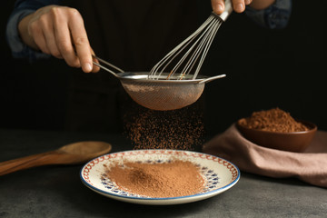 Female hands with sieve and corolla powdering cocoa onto plate