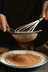 Female hands with sieve and corolla powdering cocoa onto plate