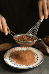 Female hands with sieve and corolla powdering cocoa onto plate