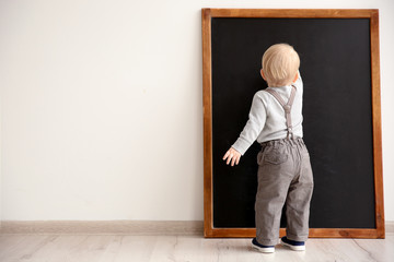 Cute little boy writing on blackboard in classroom