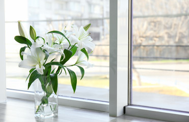 Vase with beautiful white lilies on windowsill