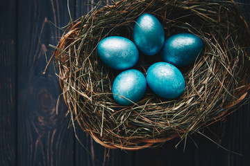 Easter colored eggs in nest on rustic wooden planks. Top view, low light photography