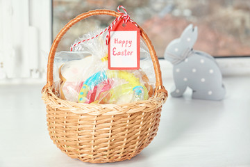 Fototapeta na wymiar Easter basket with presents, sweets and greeting card on windowsill