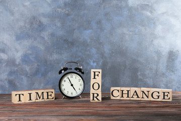 Cubes with text TIME FOR CHANGE and retro alarm clock on table against color wall