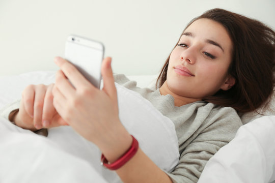 Young woman with sleep tracker and mobile phone lying in bed at home