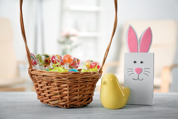 Fototapeta na wymiar Traditional Easter basket with colorful treats, ceramic bird and gift bag on wooden table
