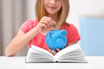 Cute girl putting coin into piggy bank at home, closeup