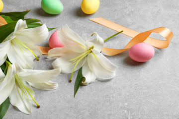 Obraz na płótnie Canvas Beautiful lilies, eggs and ribbon on gray background