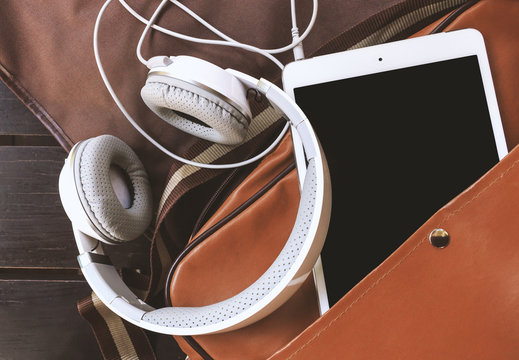 closeup headphones and tablet computer in bag on wooden table with soft-focus in the background. film colors tone