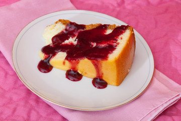 A slice of cheesecake with raspberry sauce on a white plate with a pink napkin and place mat.