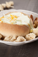 Creamy Broccoli Cheddar Soup in Large Baked Homemade Roll on white plate on dark wooden background 