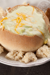 Creamy Broccoli Cheddar Soup in Large Baked Homemade Roll on white plate on dark wooden background angled macro shot