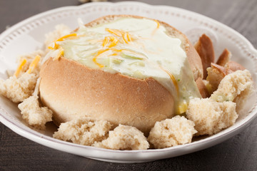 Creamy Broccoli Cheddar Soup in Large Baked Homemade Roll on white plate on dark wooden background full view of plate