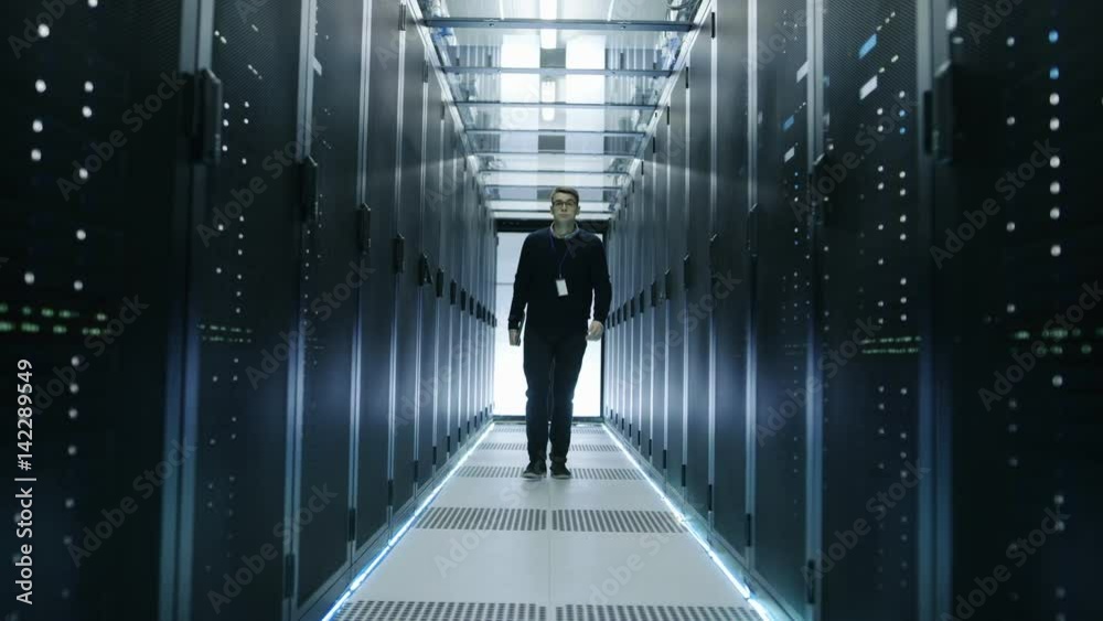 Wall mural Frontal View of IT Engineer Walking Through Data Center with Working Rack Servers.   Shot on RED EPIC-W 8K Helium Cinema Camera.