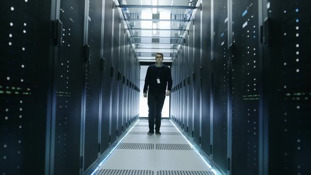 Frontal View of IT Engineer Walking Through Data Center with Working Rack Servers.   Shot on RED EPIC-W 8K Helium Cinema Camera.
