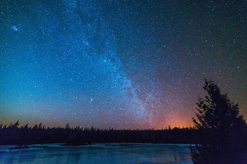 Frozen pond in winter at night with the milky way and stars