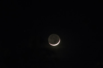 Earth shine of a crescent moon showing moon in shadow and stars. Long exposure photograph. Image contain certain grain or noise and soft focus.