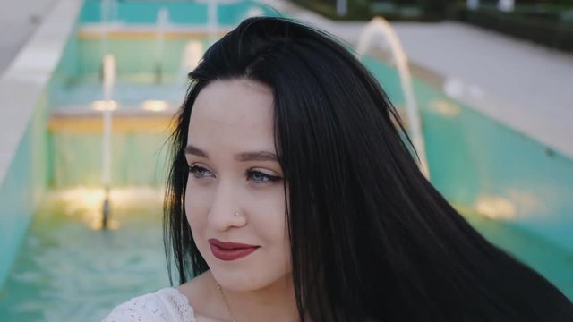 Portrait of flirting young woman. Cheerful happy girl flipping and touching her hair on illuminated fountain background.