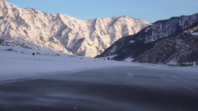 Drifting snow over winter Altai road, in Chemal Region with snow covered mountain range on background