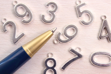 Pen and different metal numbers  on a white wooden table
