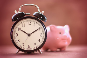 Old fashioned alarm clock with blurred piggy box and vignette