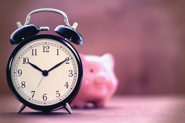 Old alarm clock with blurred piggy bank on a beautiful background